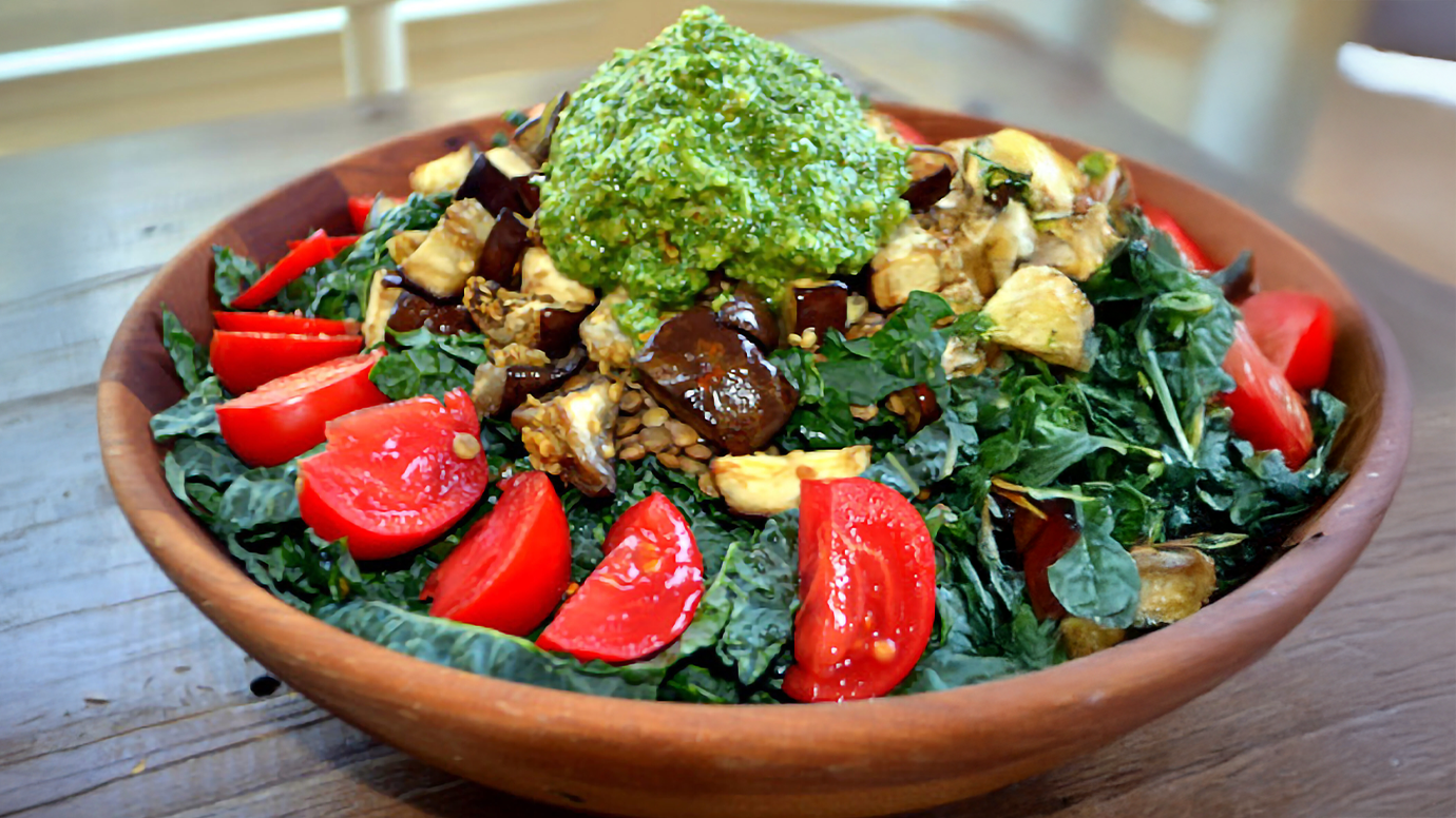 A large kale salad with tomatoes, lentils, and pesto.