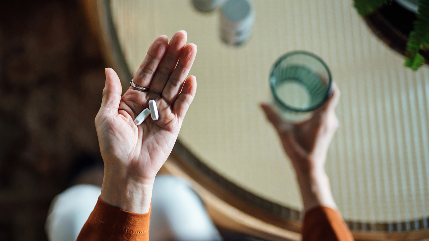 Two oral medication pills in left hand, glass of water in right hand.