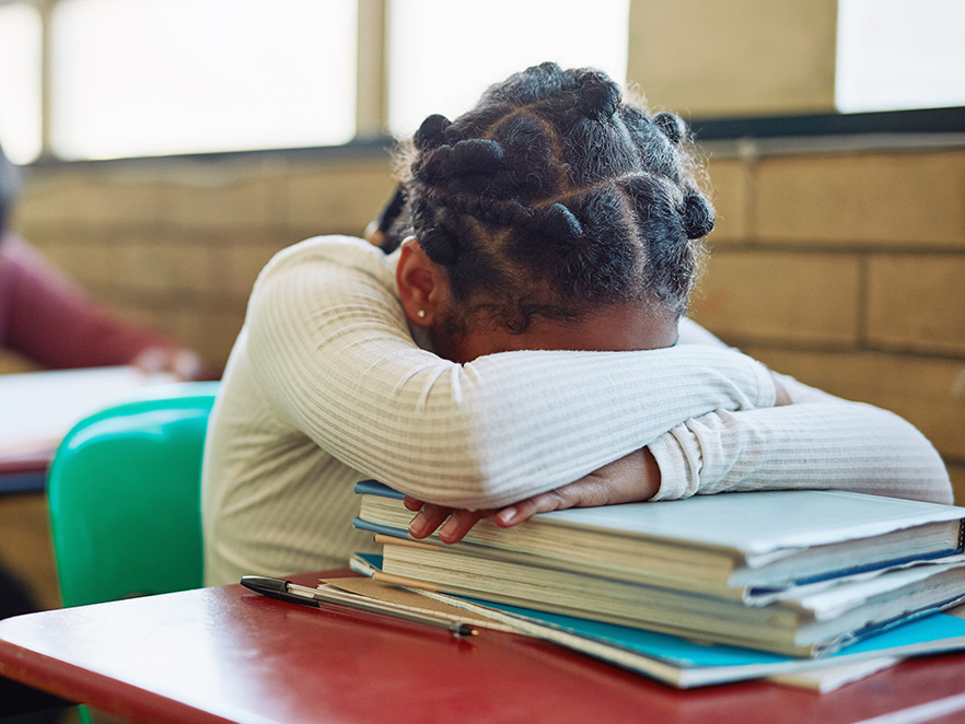 Girl in classroom puts her head on her desk.