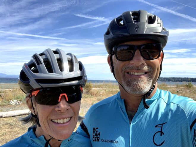 Al and Janet smile into the camera, wearing bike helmets, biking shirts, and sunglasses