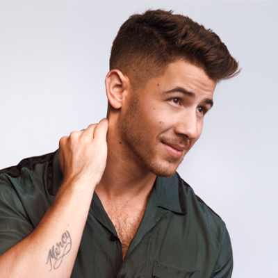 Nick Jonas looks slightly off camera, his hand rubbing the back of his neck as he smiles slightly