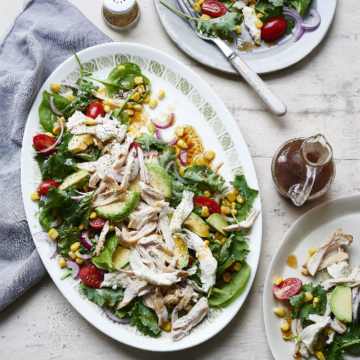 A platter of salad topped with chicken, salad, and avocados.