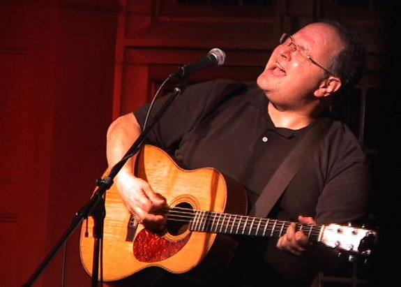 Steve Seskin sings on stage while playing the guitar.