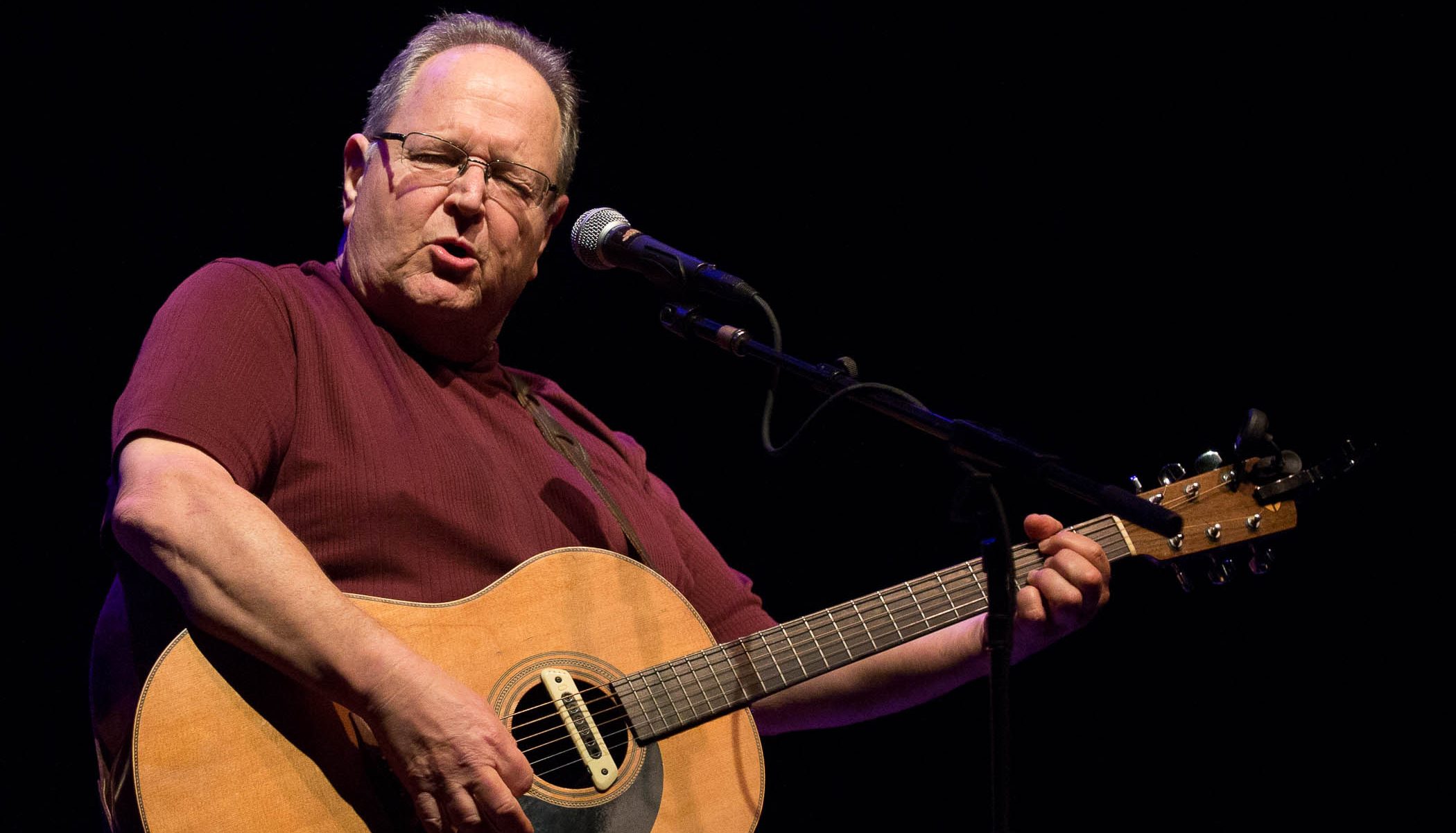 Steve Seskin sings on stage while playing the guitar.