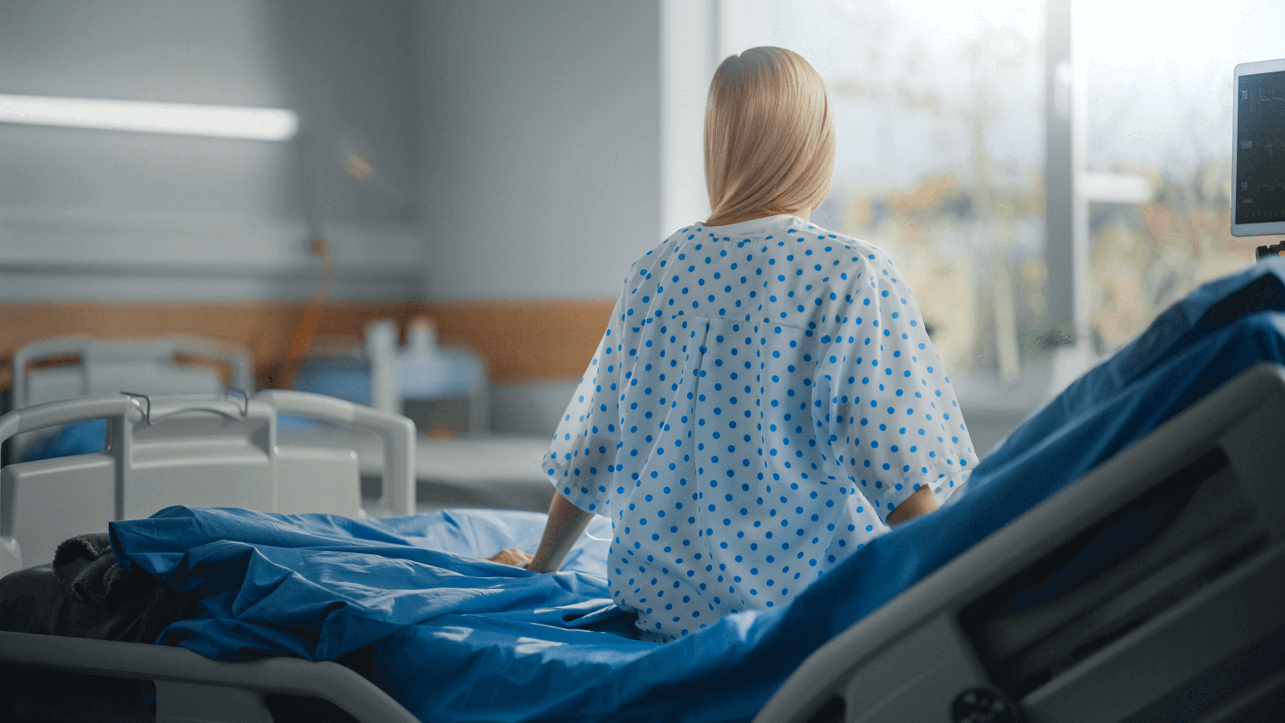 Patient sits on the edge of a hospital bed.