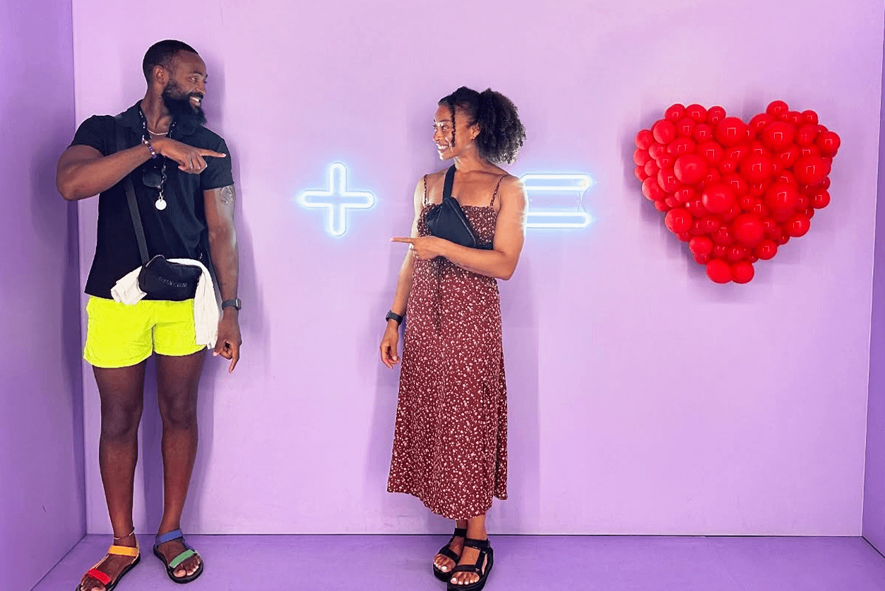 Nia and Steven pose in front installation with a plus, equal sign and heart.