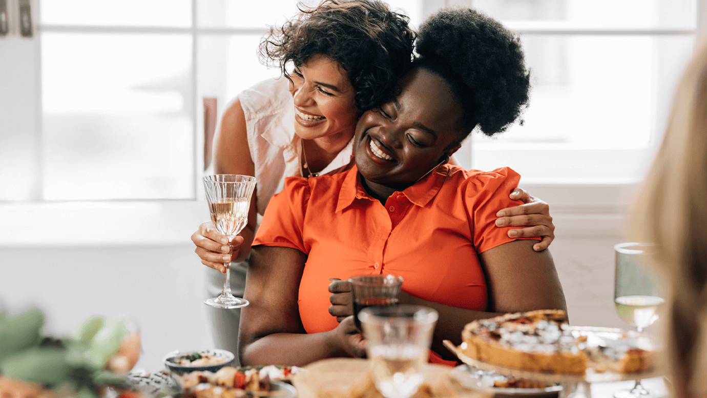 Two women embrace at a dinner table.