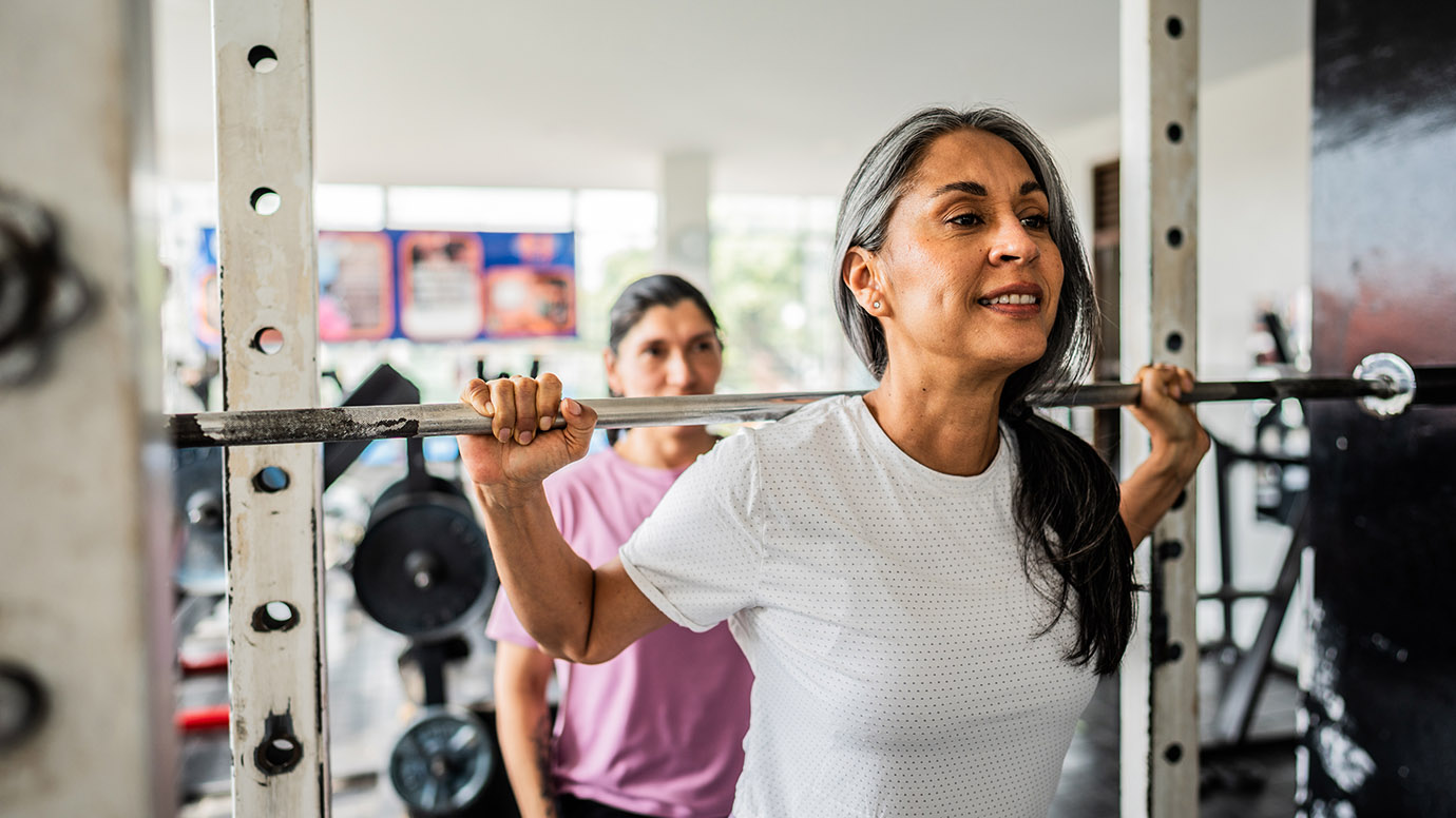 Woman lifts weights assisted by a spotter.